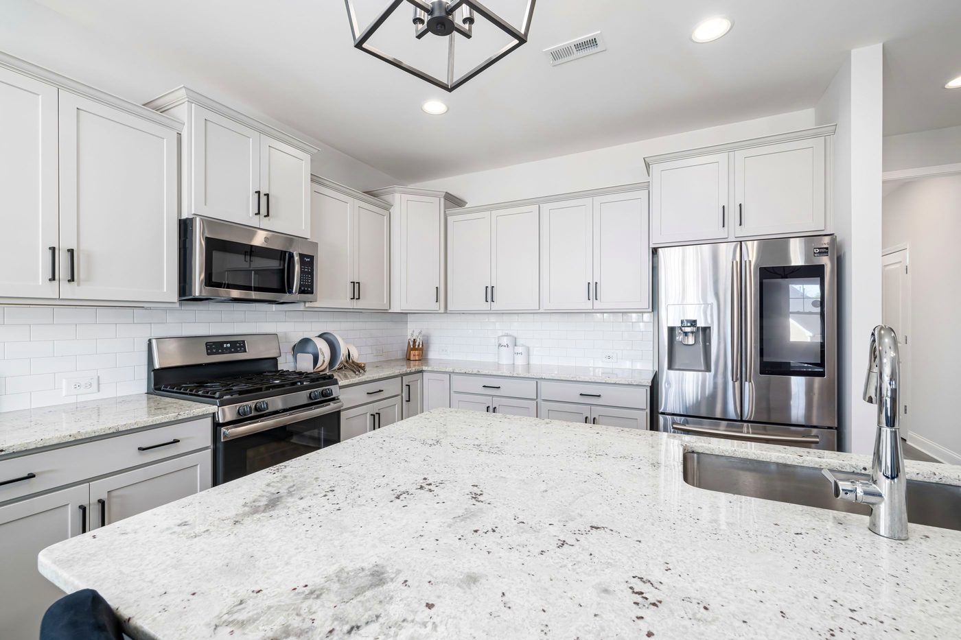 A finished kitchen with a granite island, white shaker cabinets, a subway-tile backsplash and stainless steel appliances.