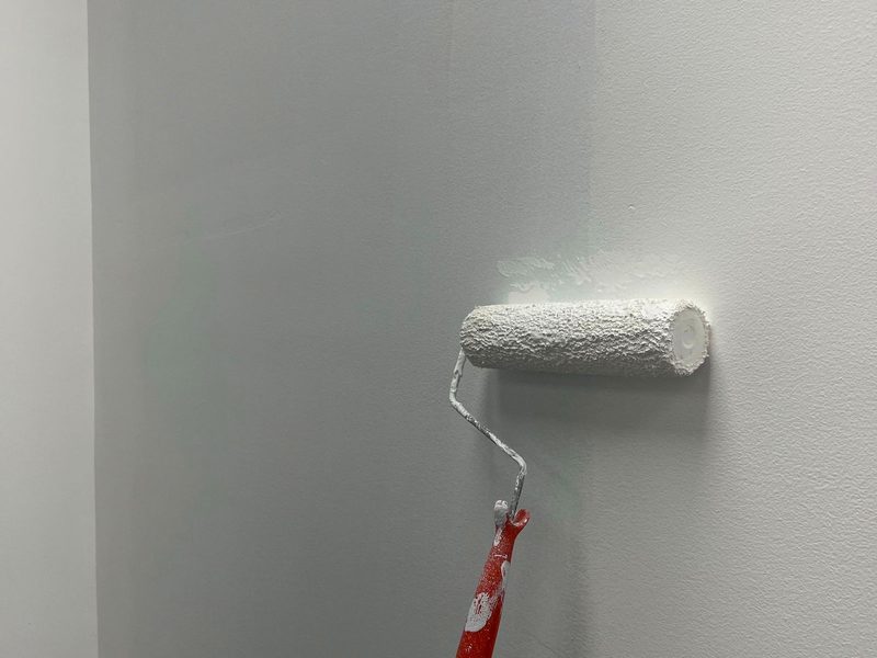 A roller laying fresh white paint onto a smooth interior wall.